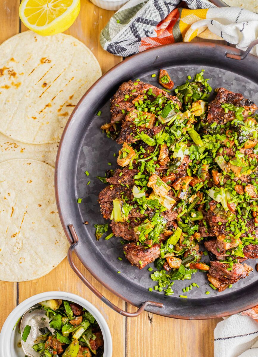 Corn tortillas are placed next to. large portion of steak and fresh herb topping. 