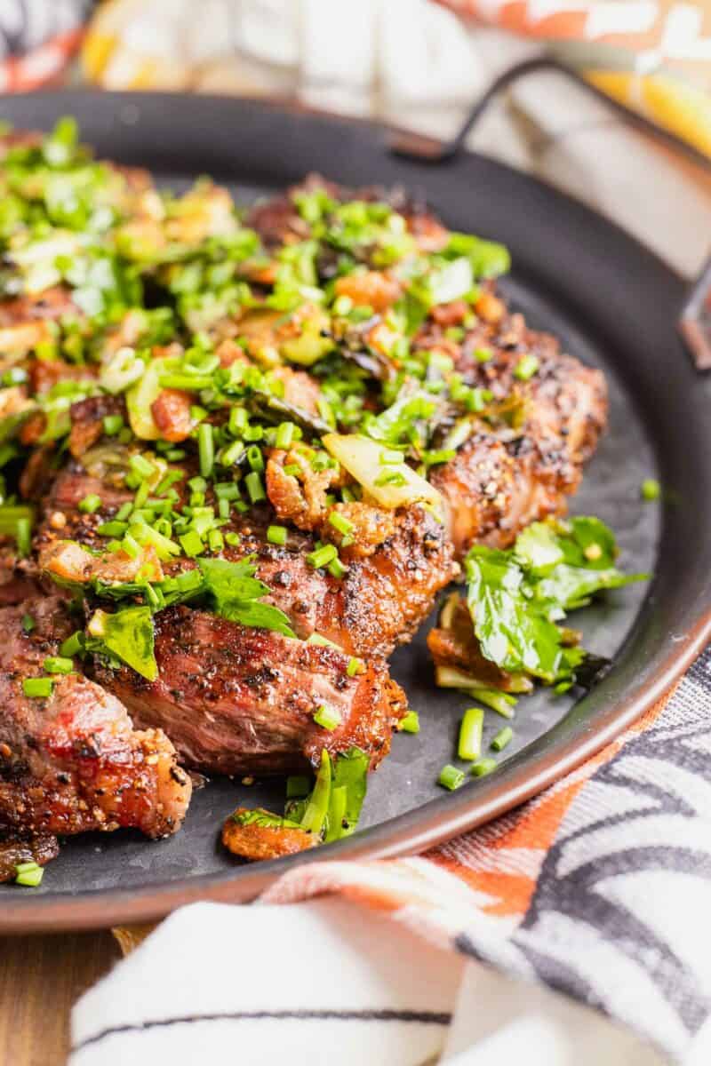 Fresh green herbs like cilantro are placed on top of a cut steak.