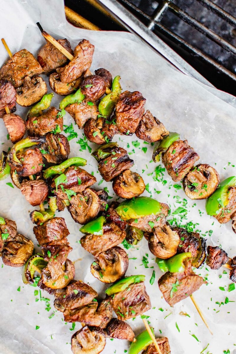 Several steak kebobs are placed on a sheet of white parchment paper. 