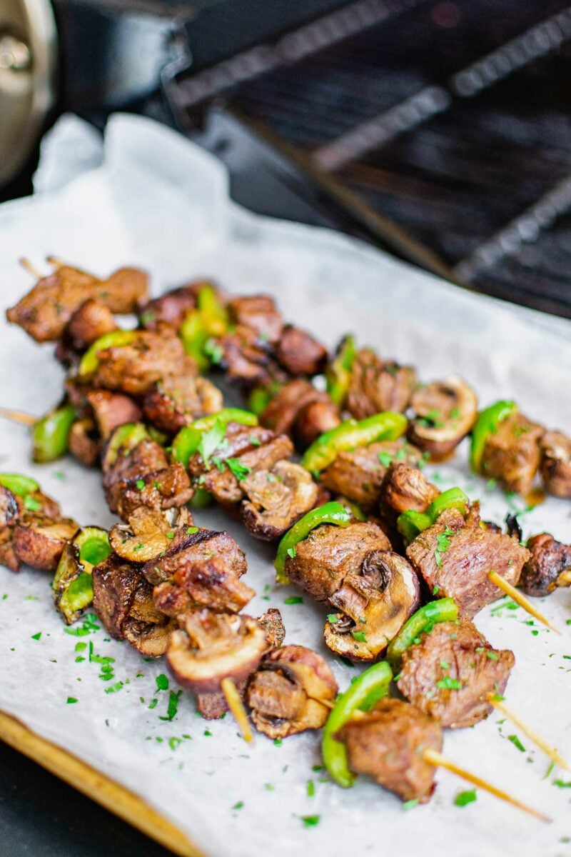 Six steak kebobs are placed on a sheet of parchment paper. 