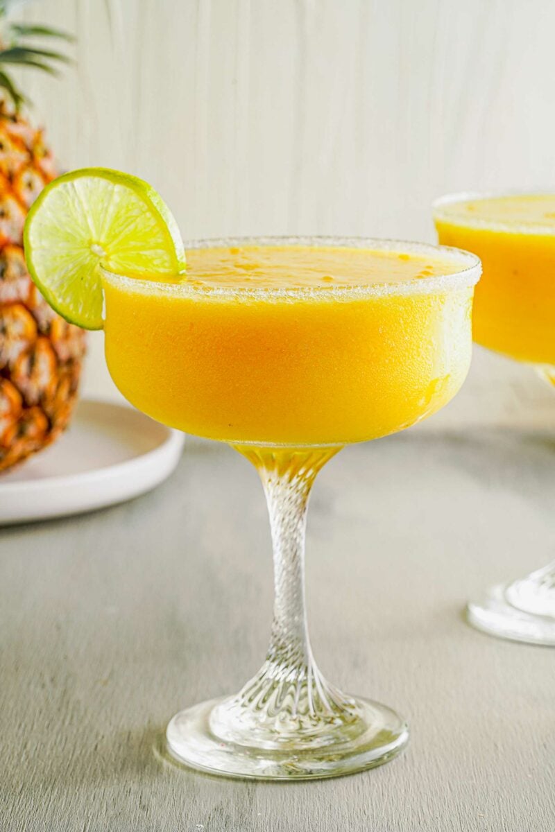 A pineapple sits behind a full glass. 