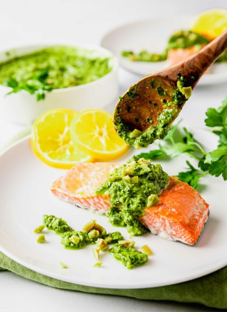 A wooden spoon is placing gremolata onto a salmon fillet. 