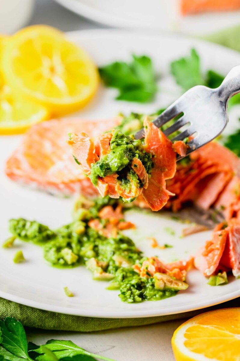 A fork is lifting a bite of salmon and garnish from the plate. 