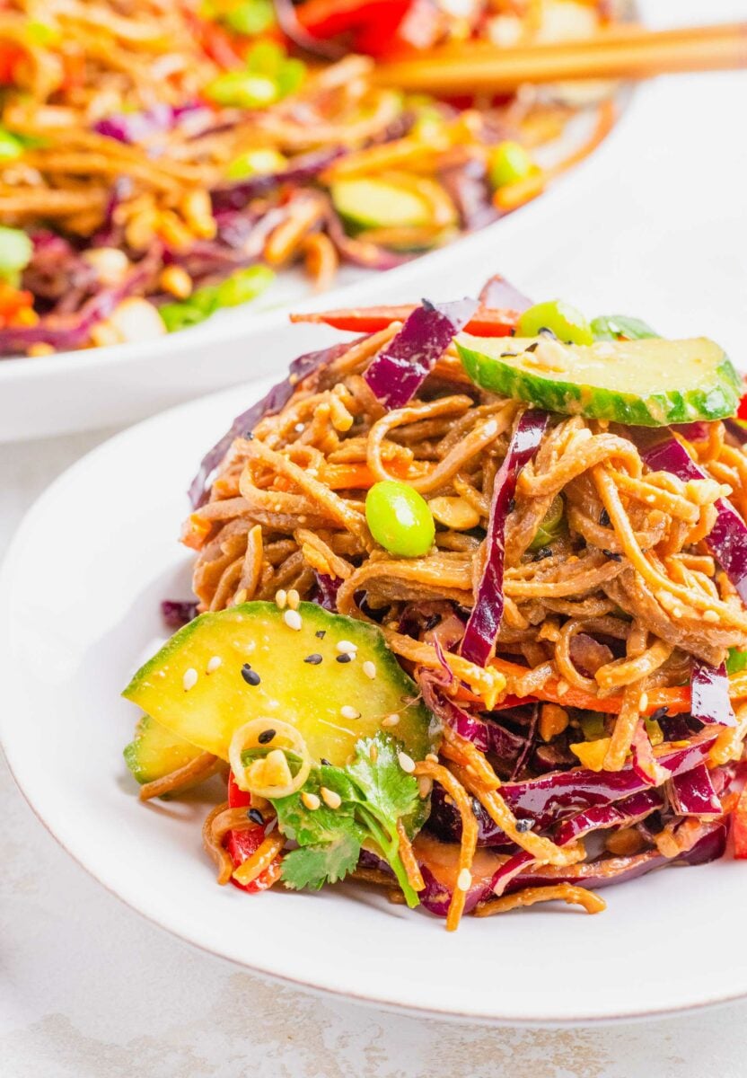 Vegetables and noodles are tossed and placed on a white plate.