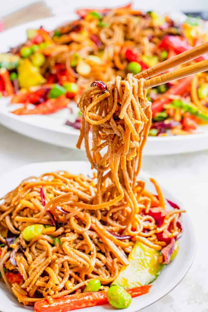 Chopsticks are lifting a bite sized potion of noodles from the bowl.