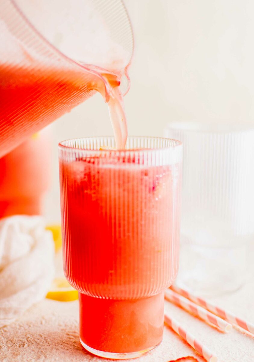 Pink lemonade is being poured into a glass from a pitcher. 