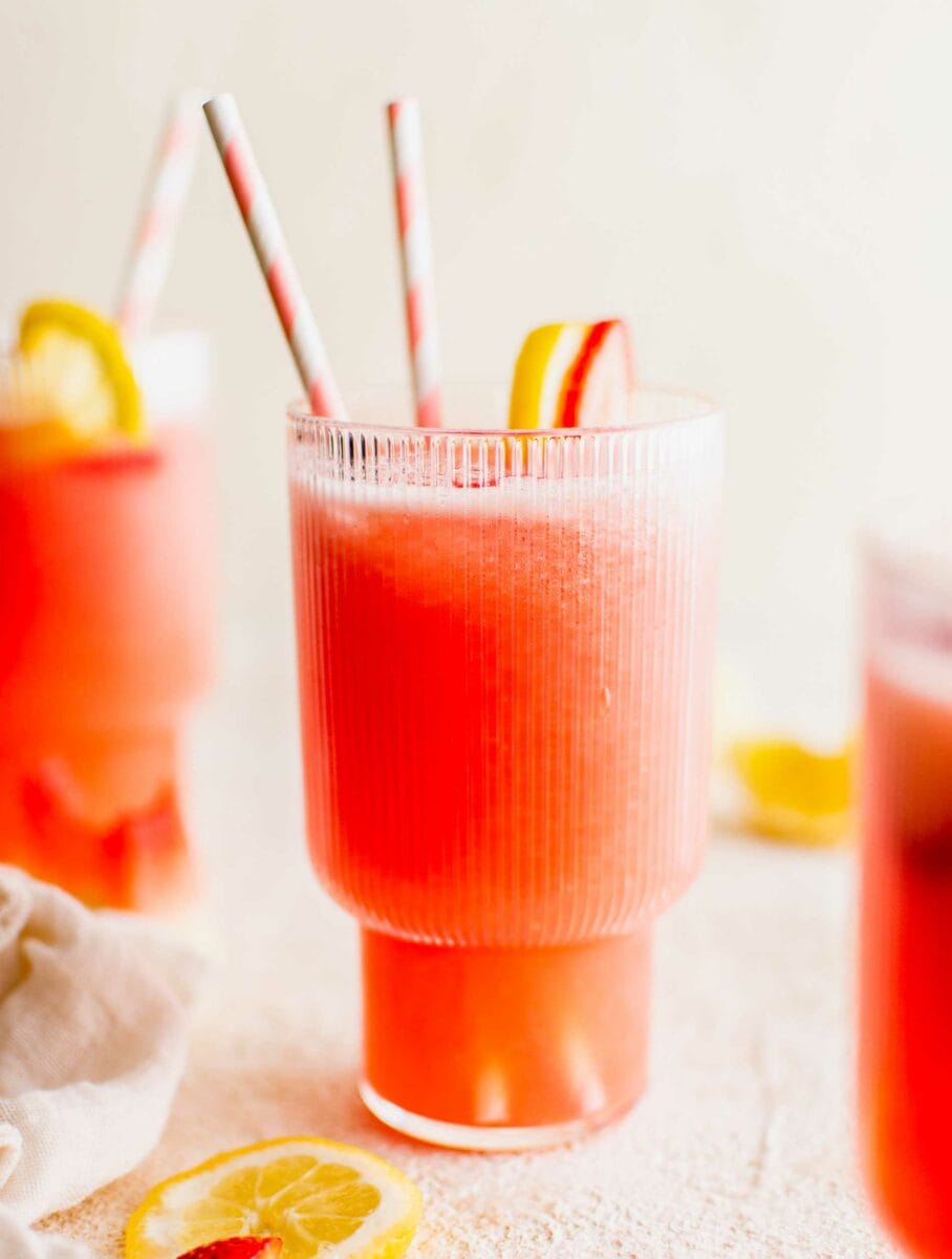 Two straws and fruity garnishes are placed in and on a glass of summer lemonade. 