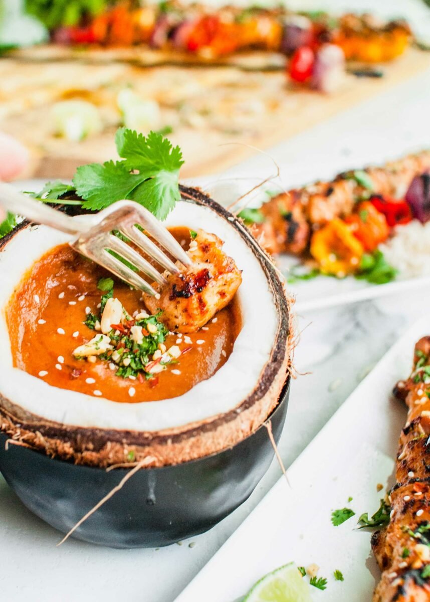 A piece of chicken is being dipped into peanut sauce. 