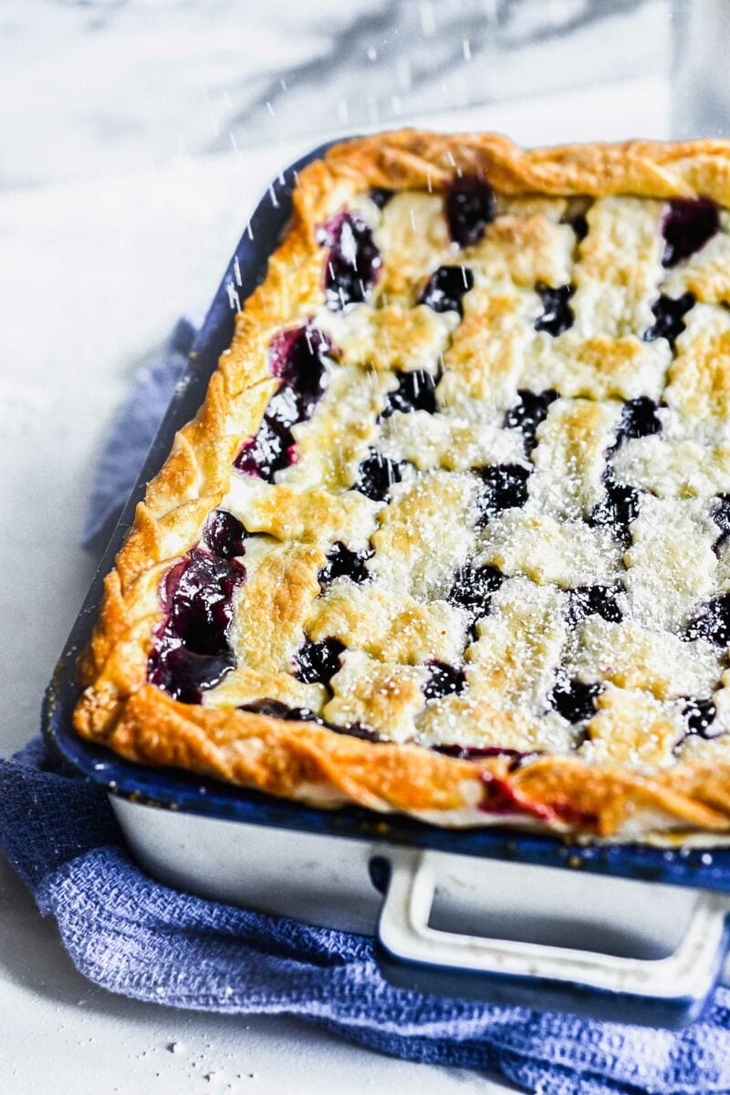 Powdered sugar is being sprinkled on top of a baked blueberry pie. 