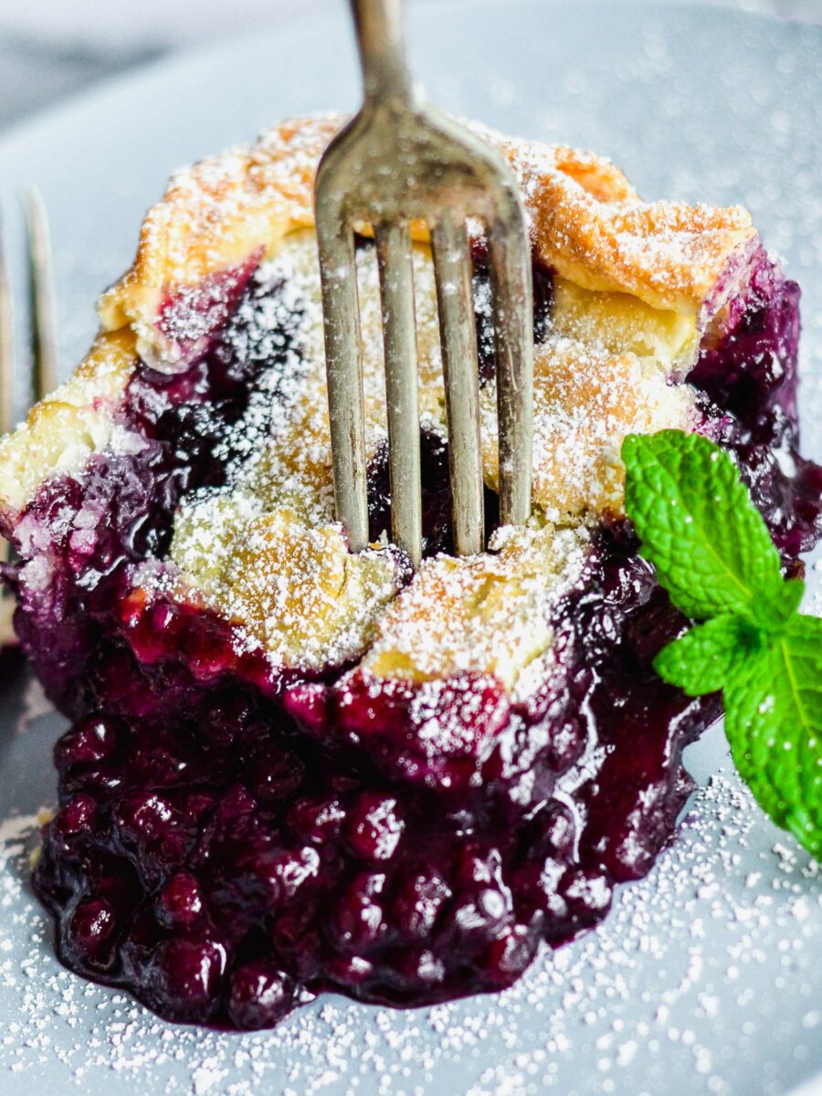 A fork is plunged into a piece of blueberry pie. 