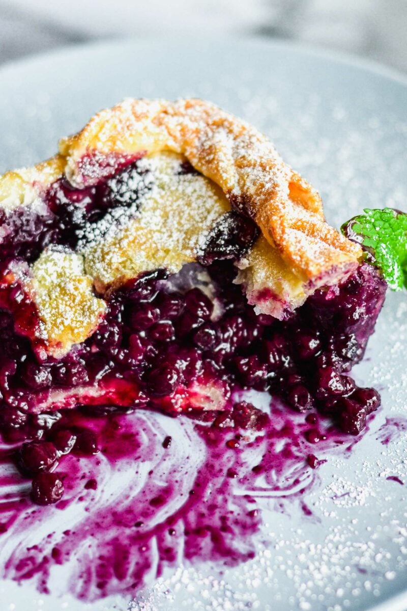 The baked blueberry pie has made a purple, juicy mess on a white plate. 