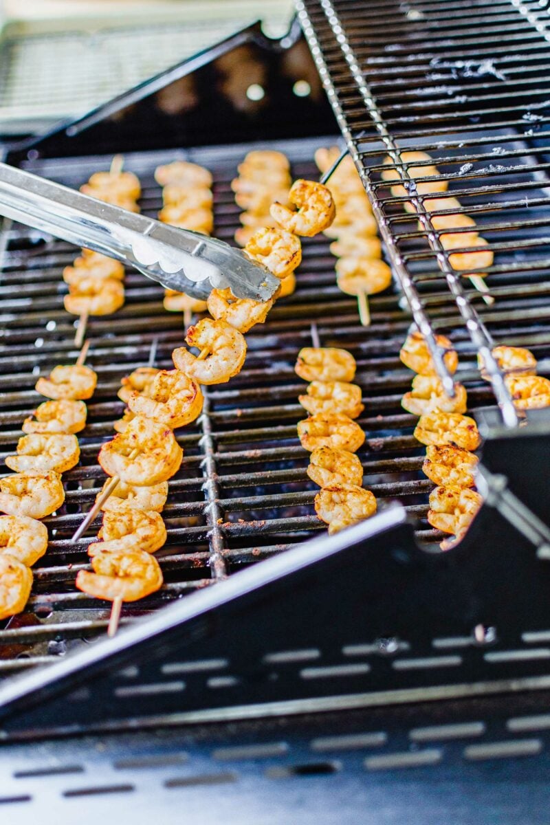 A shrimp skewer is being lifted from the grill. 