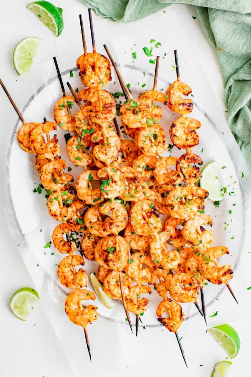 A white plate covered in parchment paper holds a large portion of shrimp skewers.