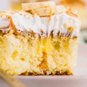 A square slice of cake is revealed with banana pudding inside and topped with whipped topping and banana slices.