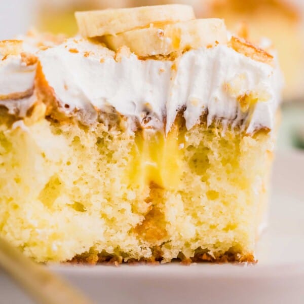 A square slice of cake is revealed with banana pudding inside and topped with whipped topping and banana slices.