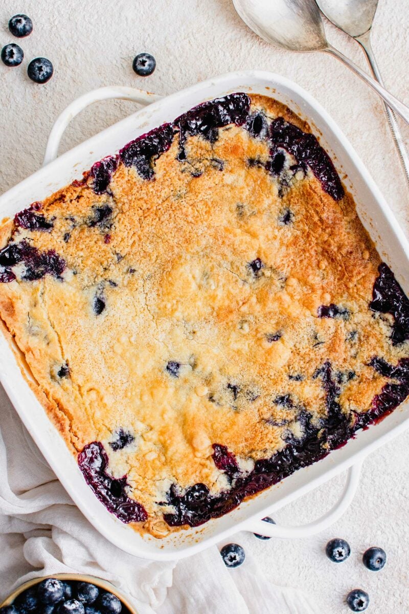 A square white dish is filled with baked blueberry dump cake. 