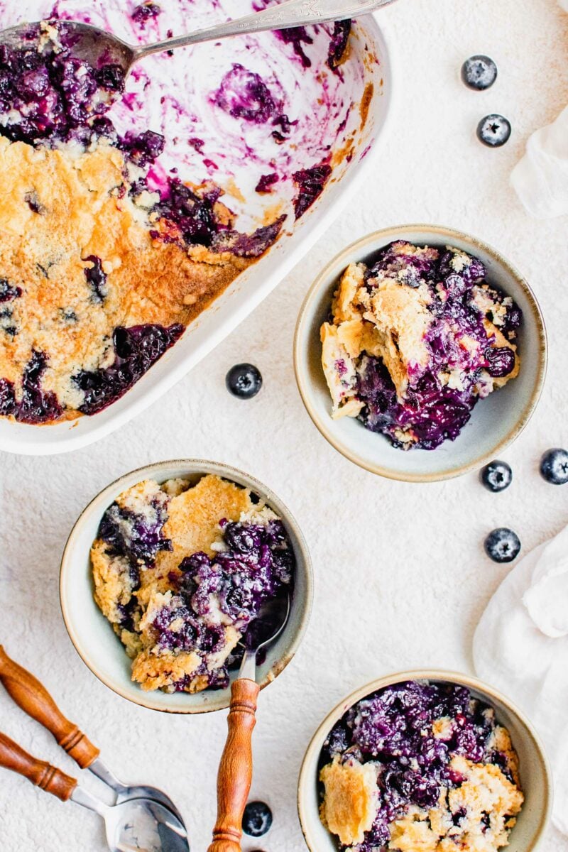 Three full bowls are placed next to a casserole dish with blueberry cake. 