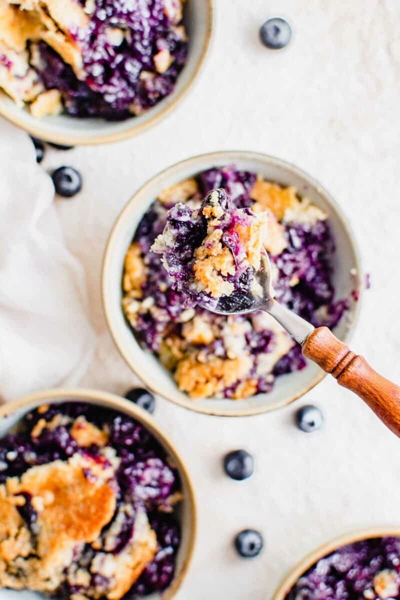 A spoon is lifting a bite of blueberry dump cake from a bowl. 
