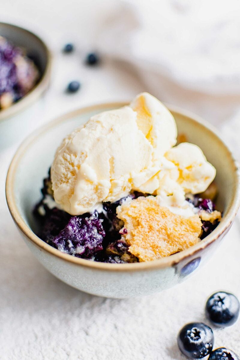 Vanilla ice cream is placed on top of a serving of blueberry dump cake. 