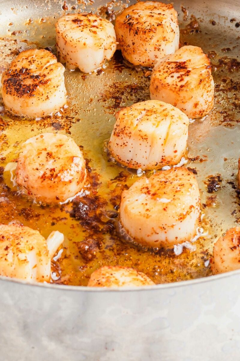 Scallops are being cooked in avocado oil in a large skillet. 