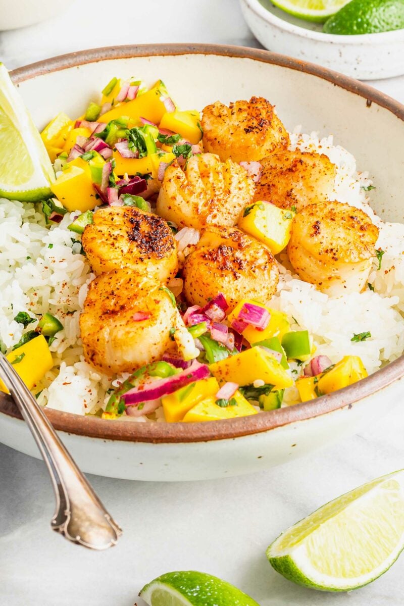 A tan and white bowl is filled with rice, relish, and scallops. 