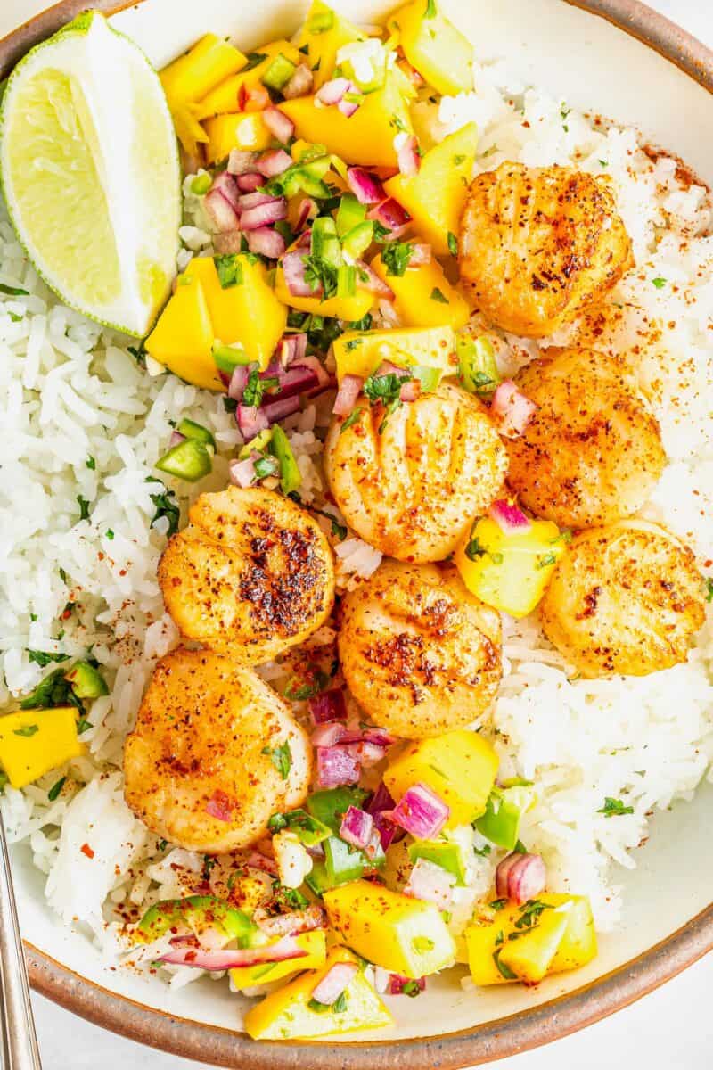 Cajun scallops are in a rice bowl with lime slices and mango relish. 