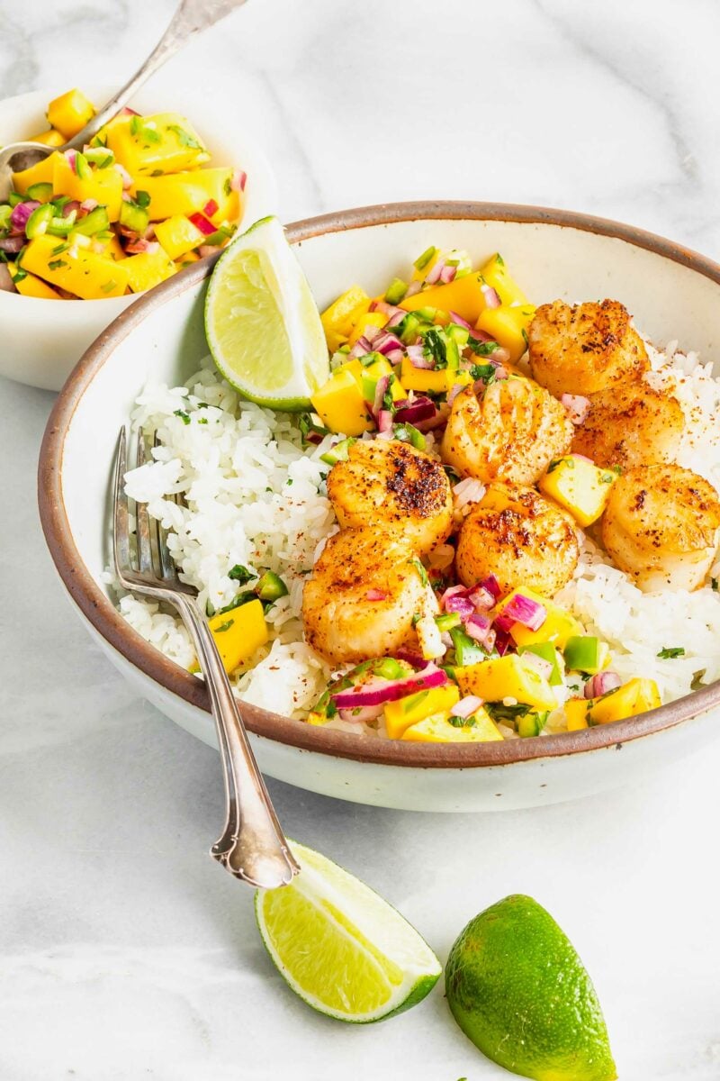 Lime wedges are placed on the outside of a rice and scallop bowl. 