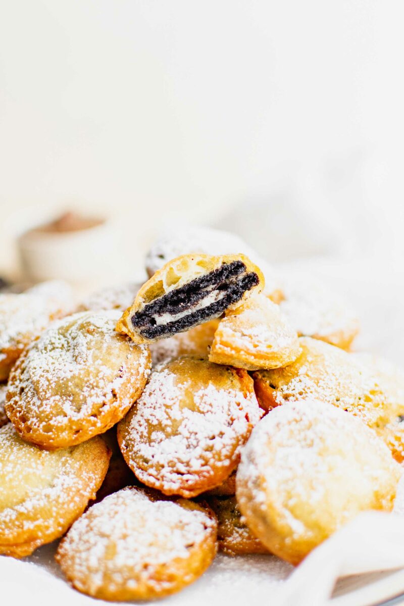 A fried oreo is cut in half on top of a stack of other fried Oreos. 