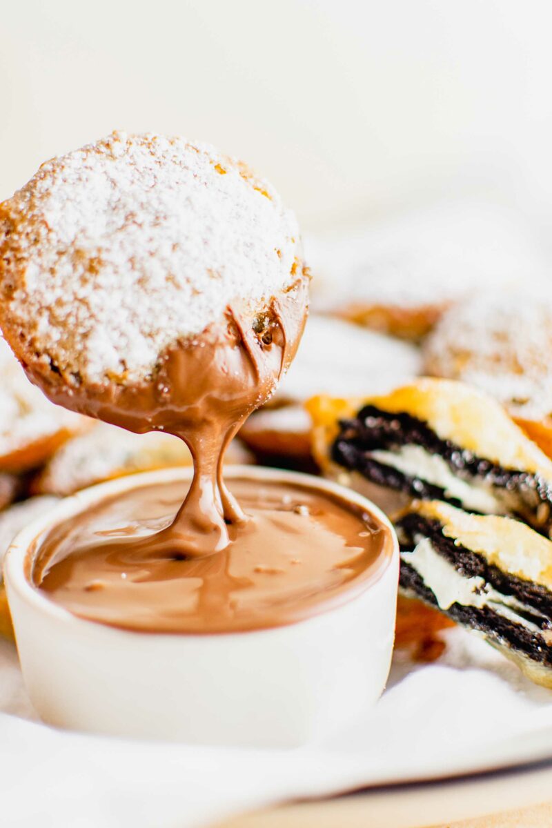 A fried Oreo is being dipped into chocolate sauce. 