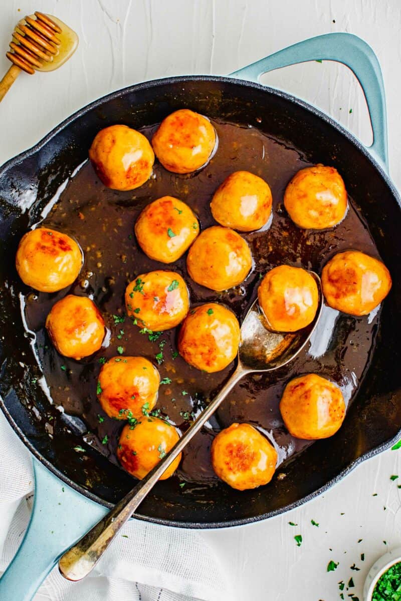 A black skillet is filled with chicken meatballs and hot honey sauce. 