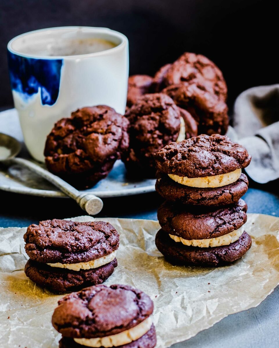 Ice cream sandwiches are placed on a sheet of parchment paper on a dark countertop. 