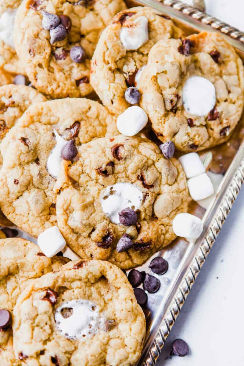 Marshmallows and chocolate chips garnish a serving platted filled with s'mores cookies. 