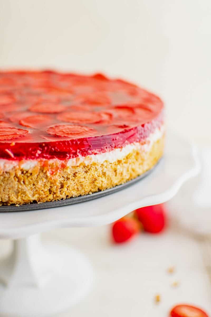 A strawberry pretzel salad is uncut and presented on a white cake stand. 