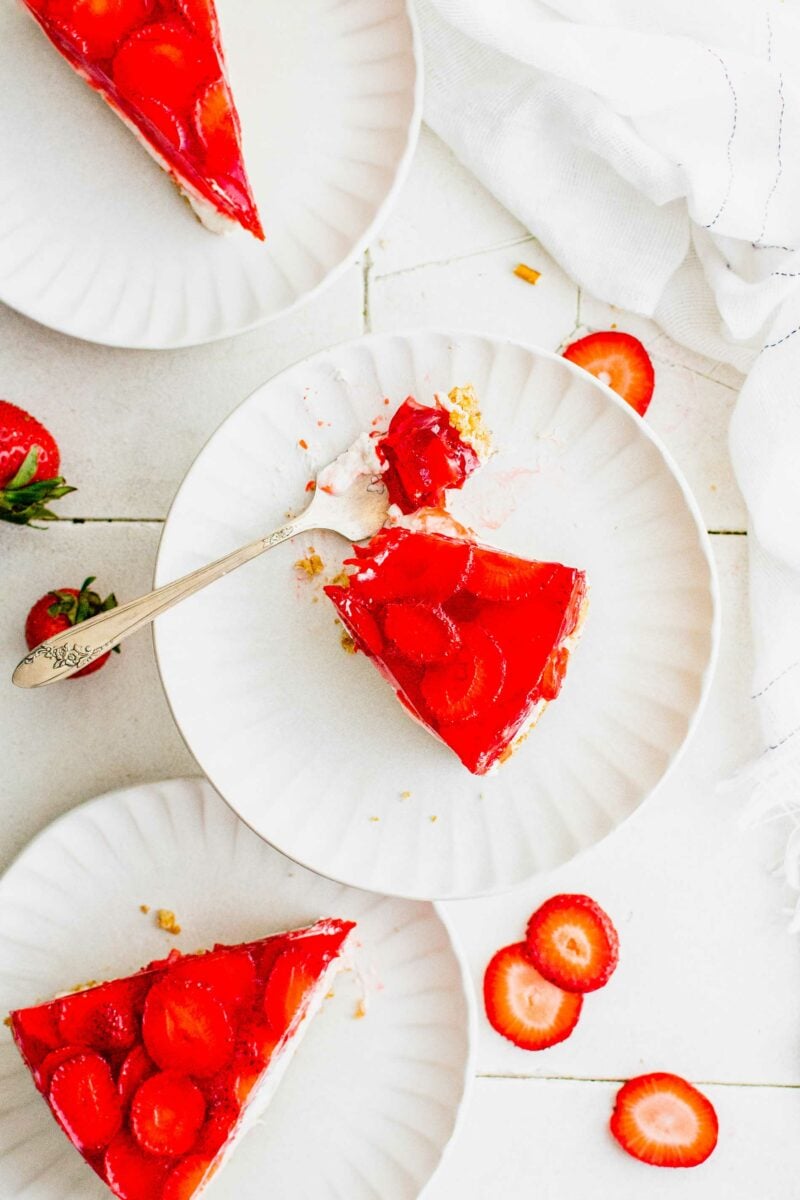 Several slices of strawberry pretzel pie are places on white plates. 