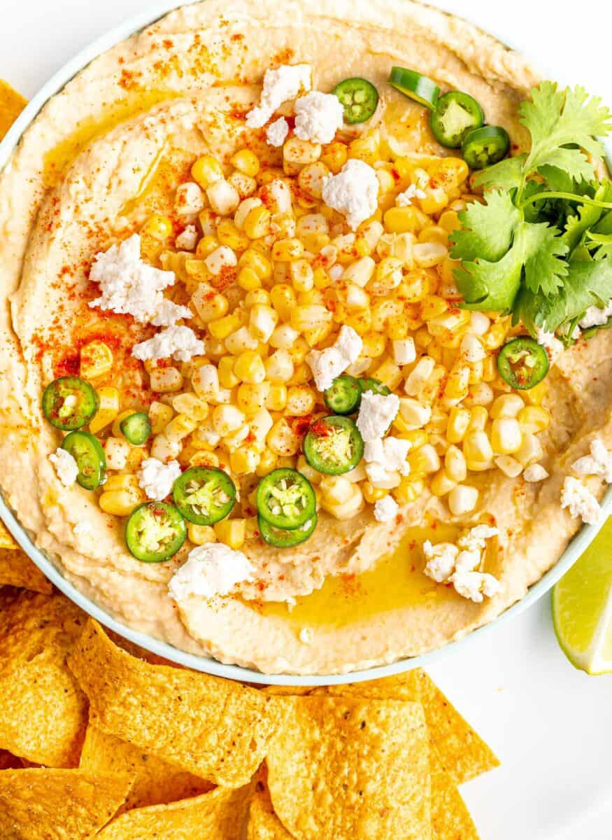 Hummus is topped with corn, cojita cheese, cilantro, and sliced Serrano peppers.