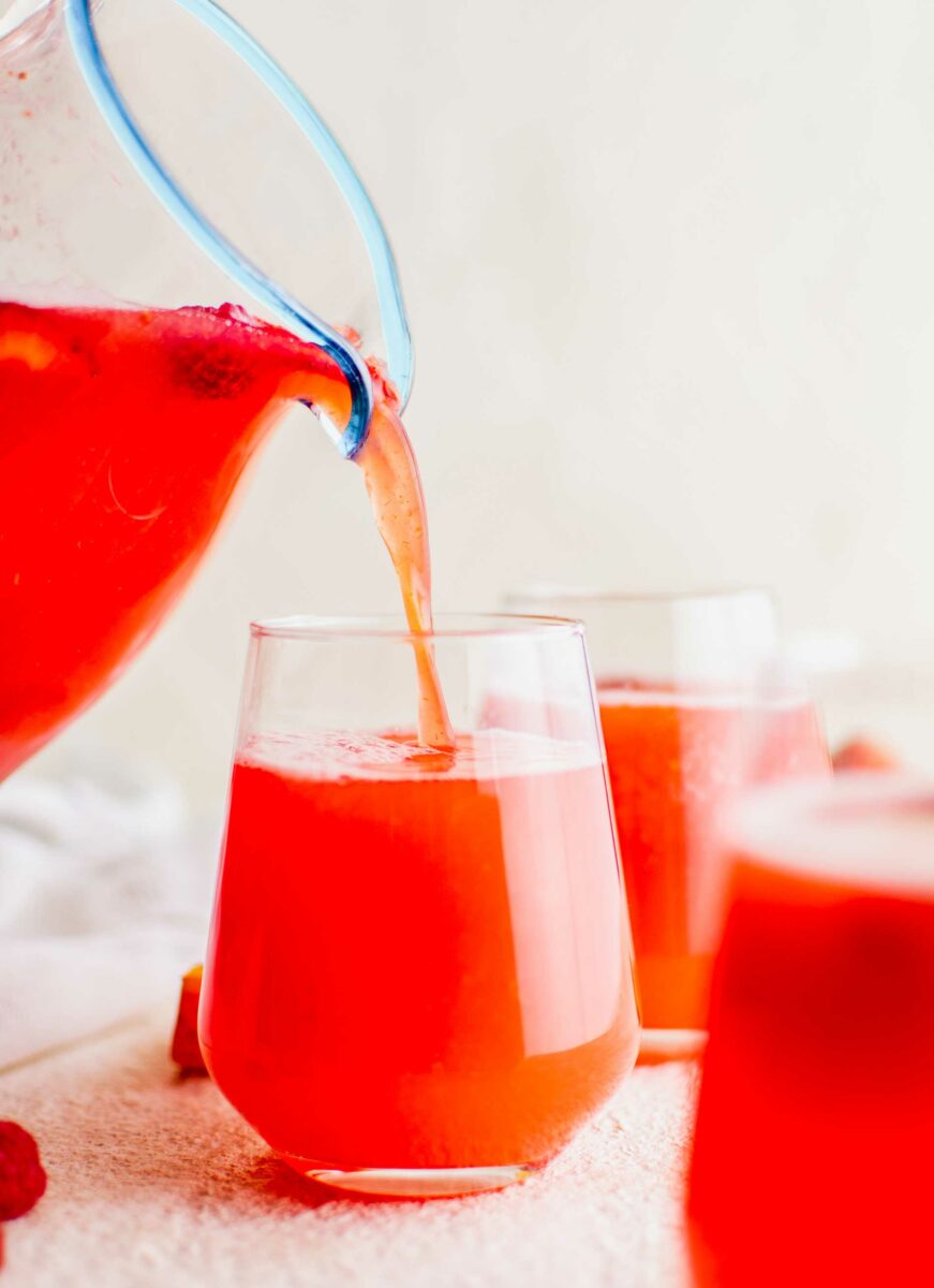 Punch is being poured from a pitcher to a small wine glass. 