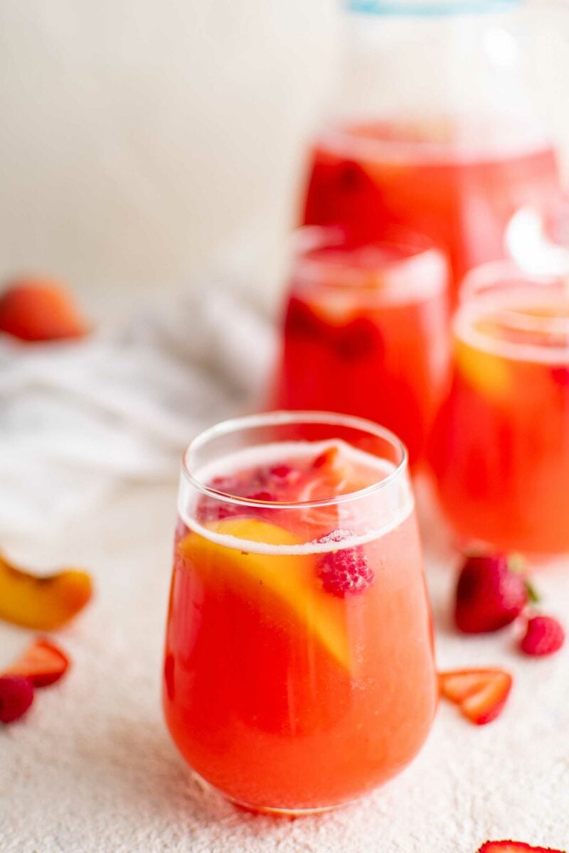 A cup of punch has fruit floating around in it. 