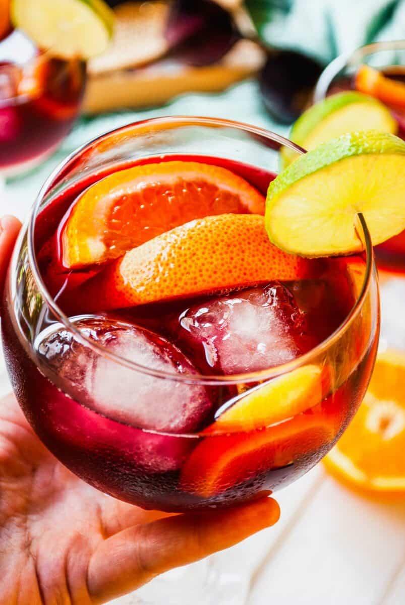 A small round glass is filled with ice cubes, wine, and fruit slices.