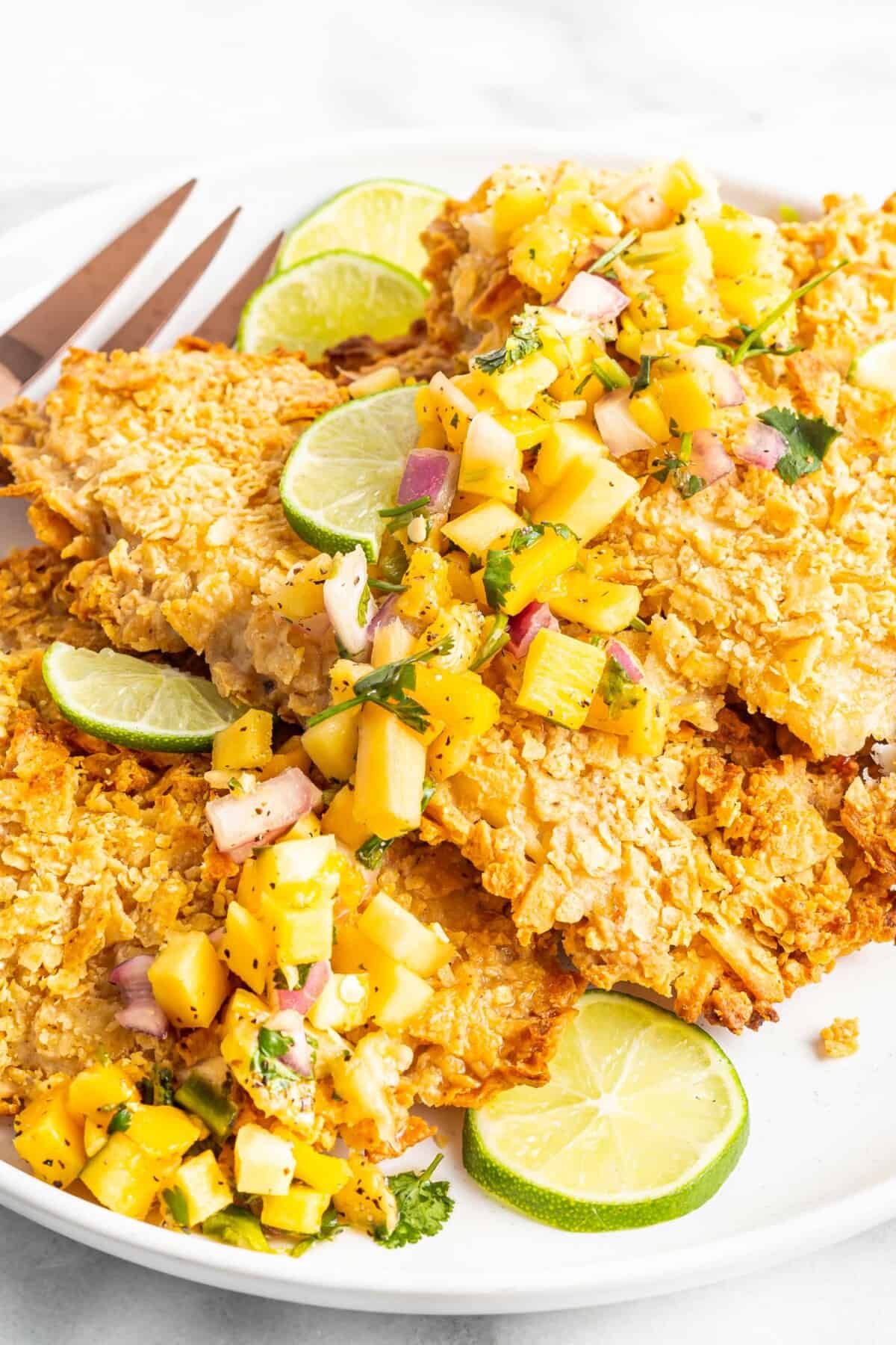 Baked tortilla crusted tilapia is garnished with limes and mango.