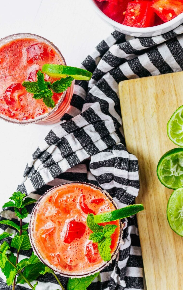 Two margaritas are placed on a black and white tea cloth. 