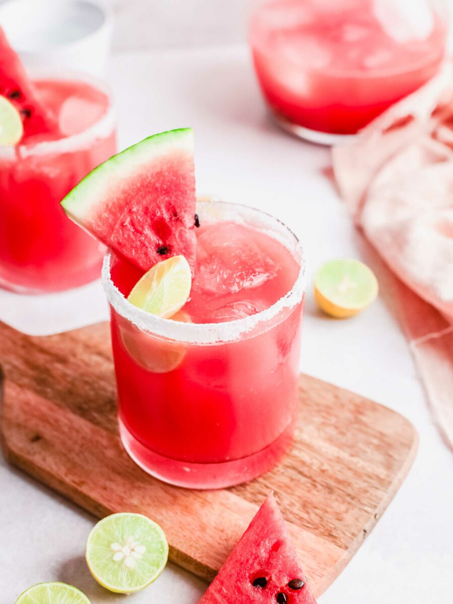 A paloma is garnished with a salt rim, lime slice, and small slice of watermelon. 