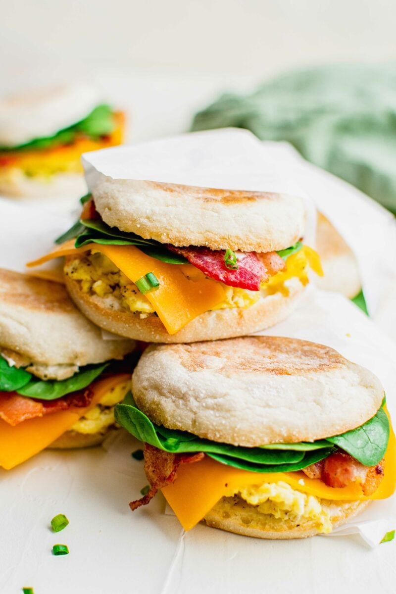 Three breakfast sandwiches with parchment paper are presented on a white surface. 