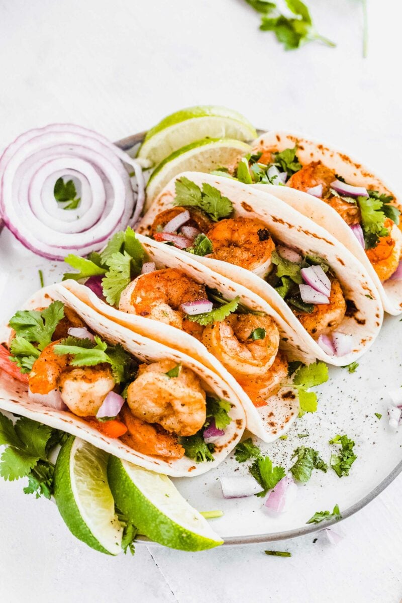 A serving of shrimp tacos is plated and ready to be eaten. 