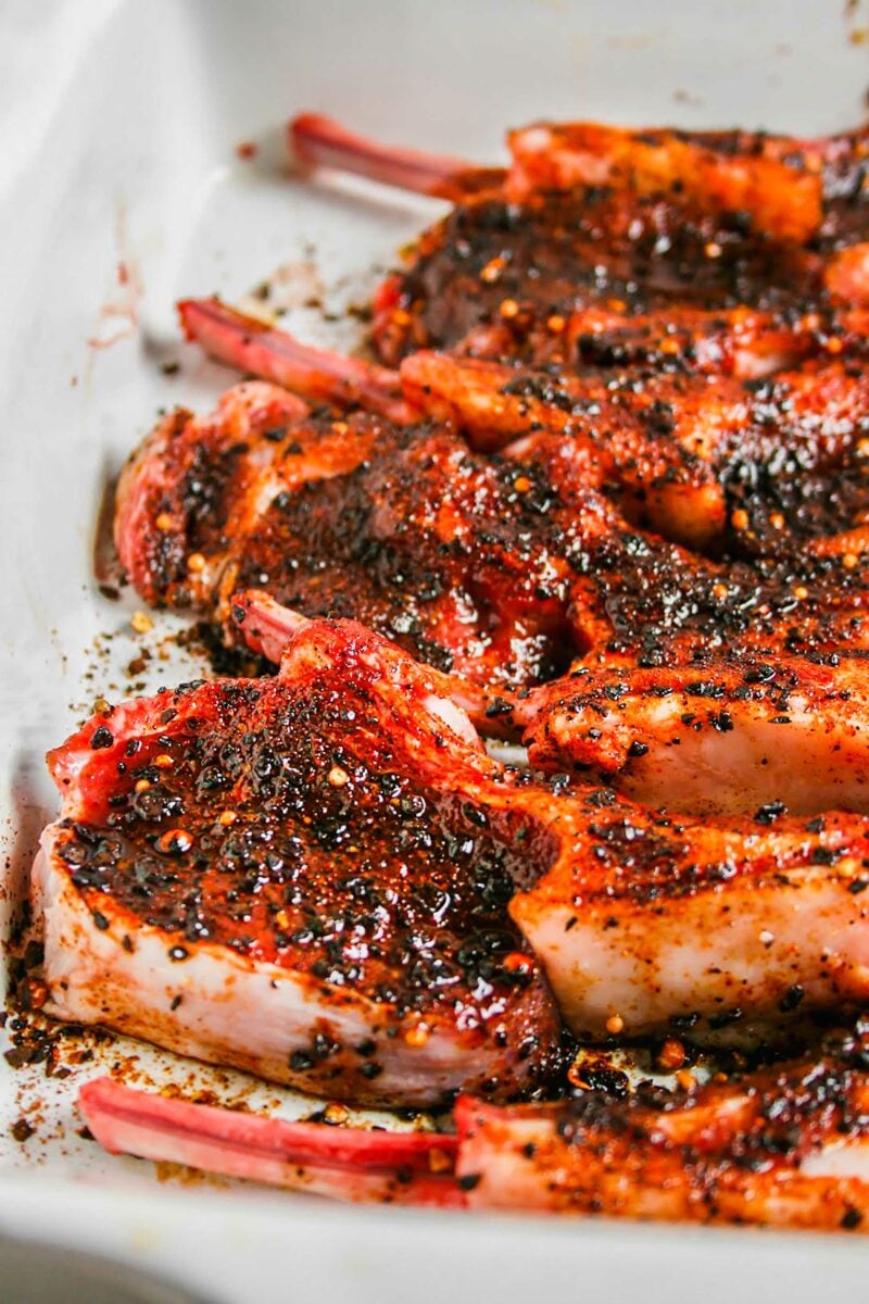 A large white serving plate is filled with multiple rubbed lamb chops. 