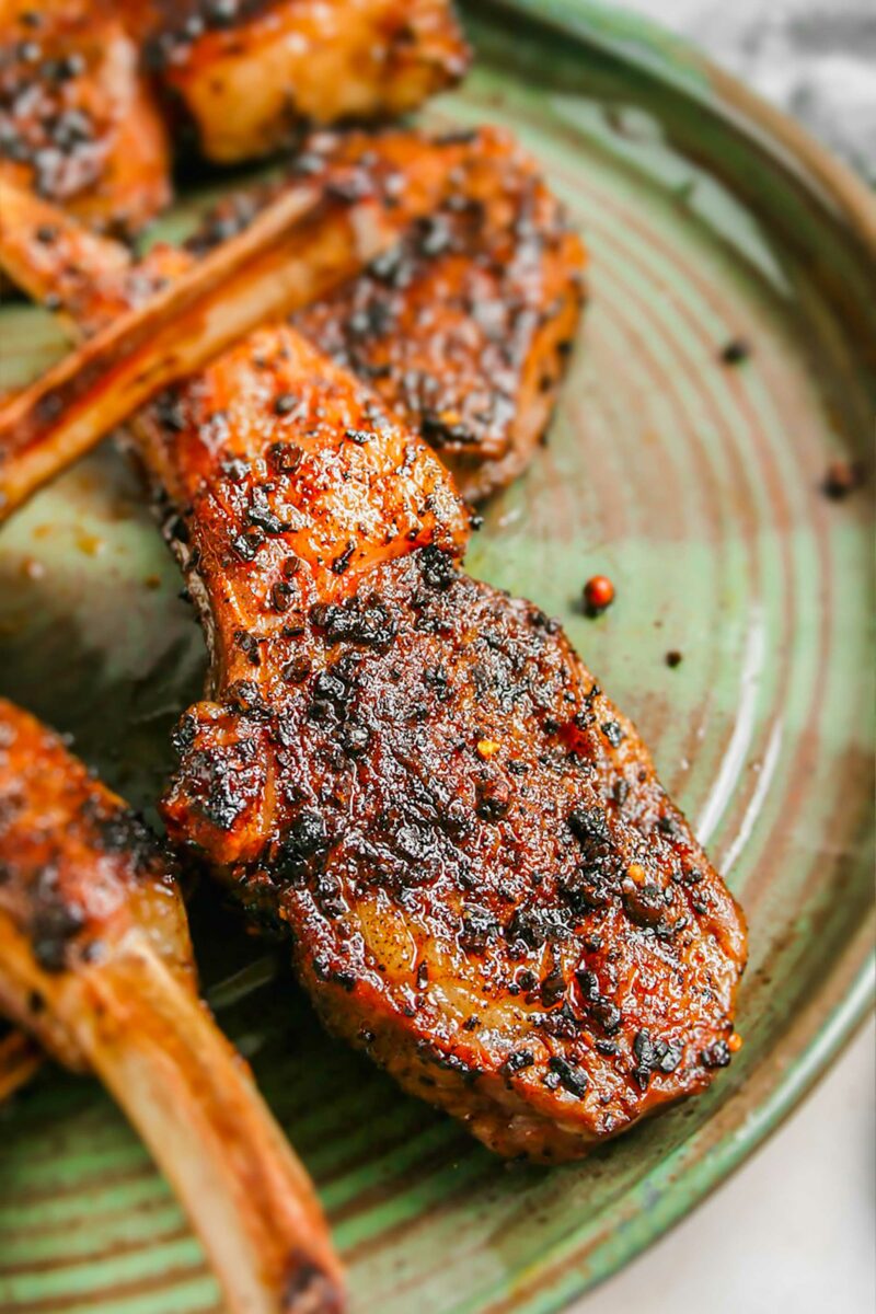 Grilled lamb chops are plated on a round green rustic plate. 