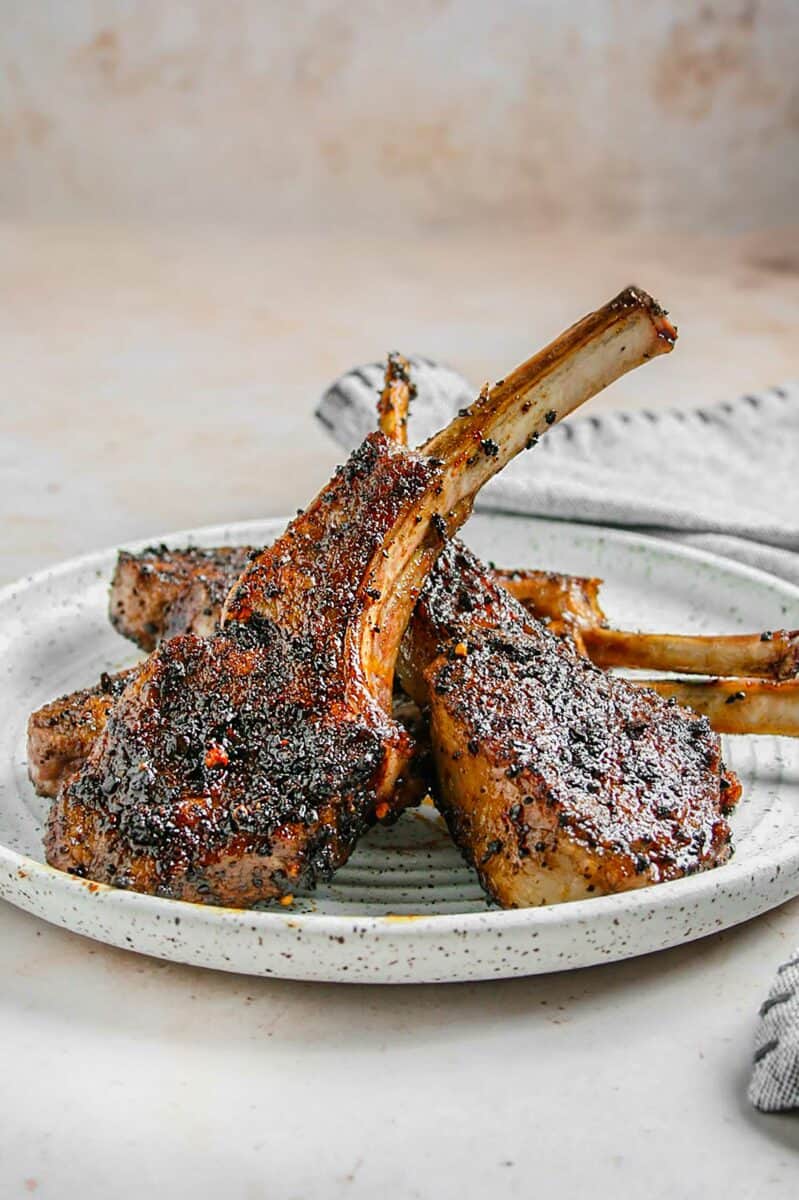 Several grilled lamb chops are presented on a spotted white plate. 