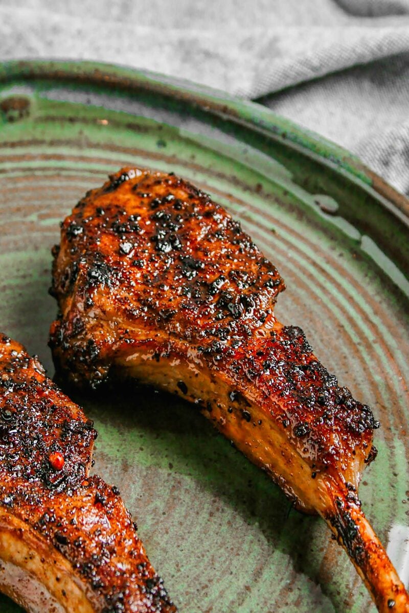 Two lamb chops are placed on a green plate. 