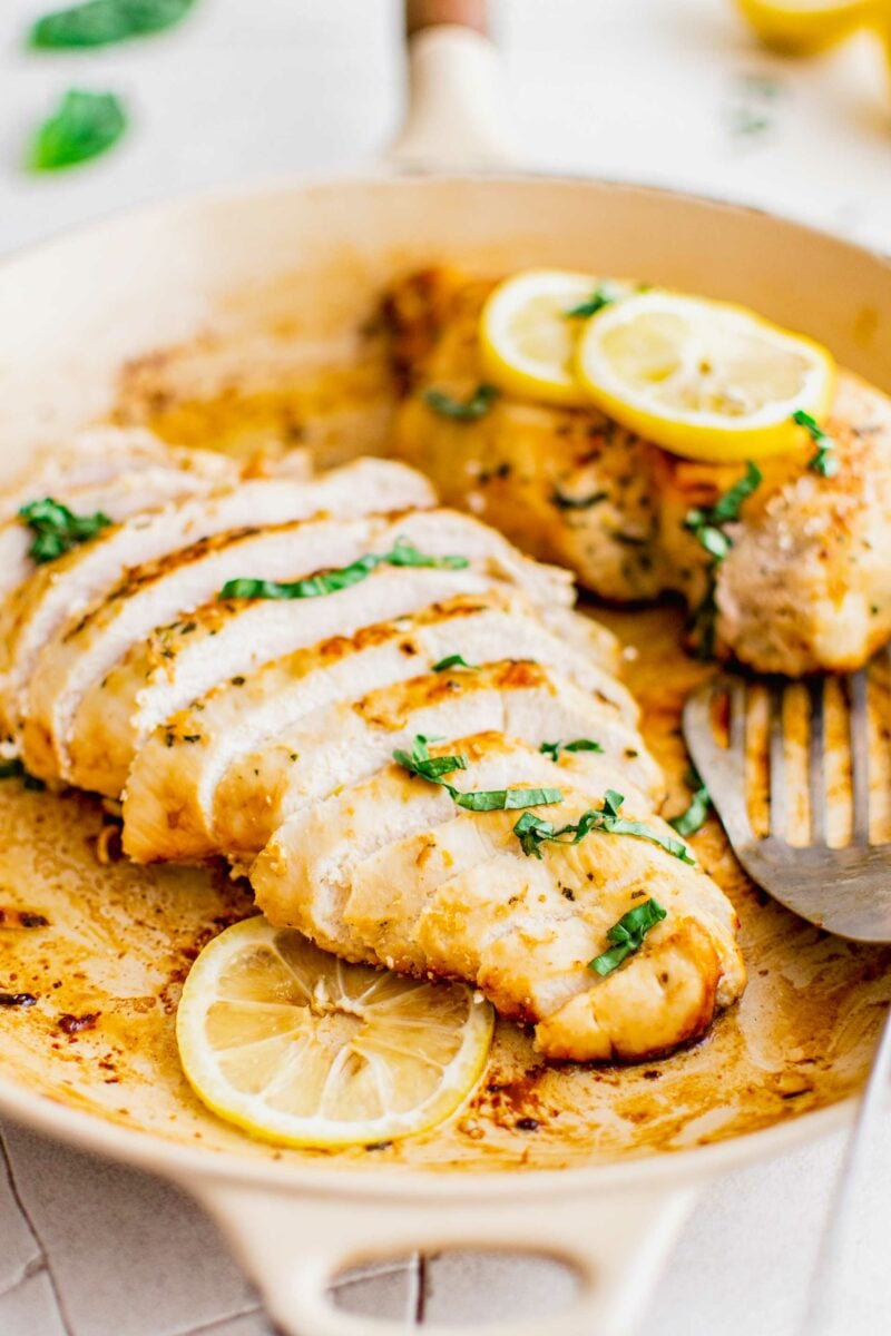 A sliced chicken breast is in a pan with lemon slices. 