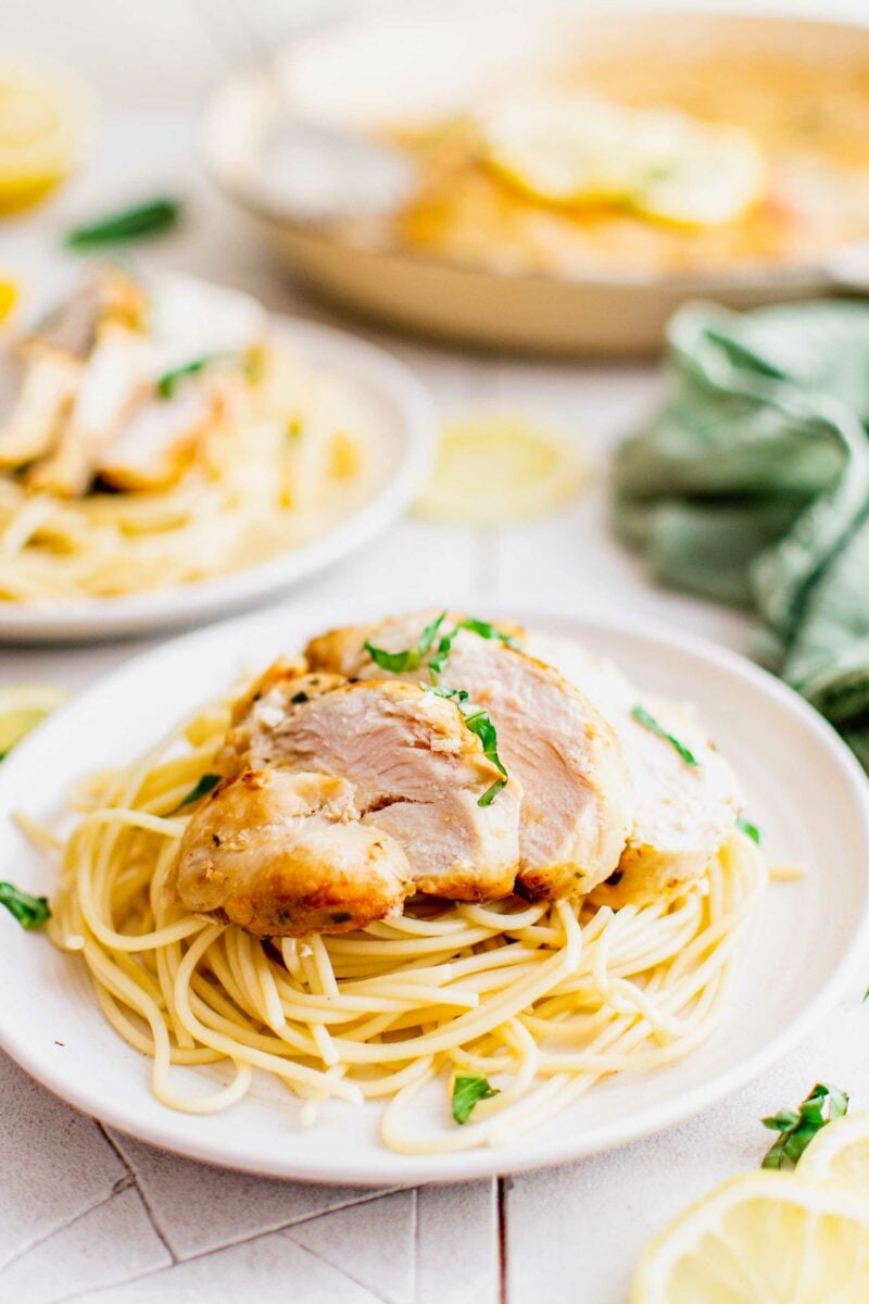 A sliced chicken breast is served over a portion of spaghetti noodles on a white plate. 