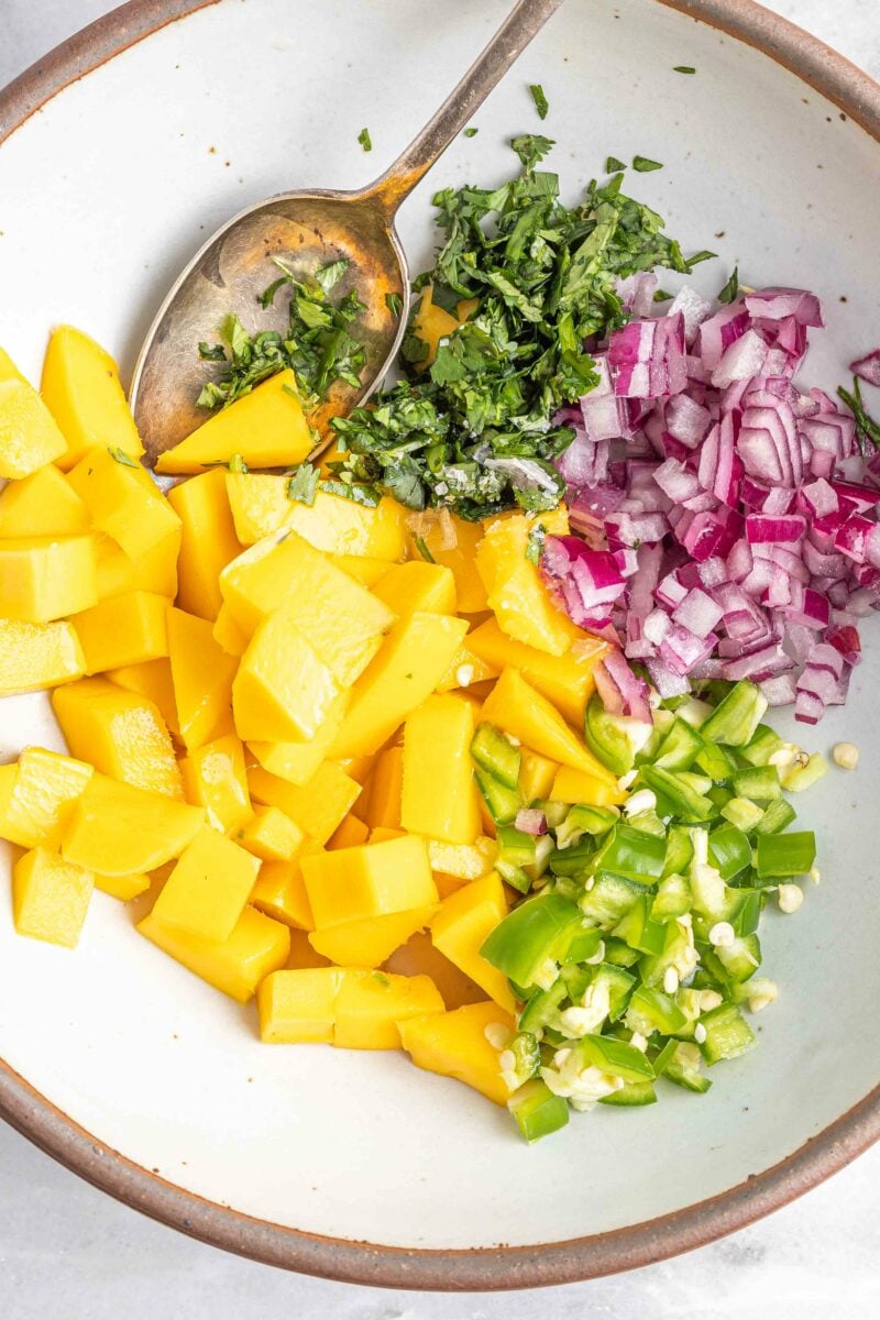 The ingredients for mango relish are not mixed in a small white bowl. 